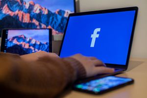 Laptop displaying Facebook at workspace with multiple devices, highlighting modern technology.
